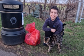 Alex by a bin, with a bag of litter, and a cat cuddling up to him