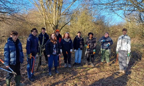 Members from the Young People's Forum standing in a woodland holding work tools and smiling at the camera