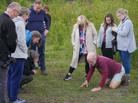 Iain, knelt on the floor examining a find on the ground, and explaining to the group around him
