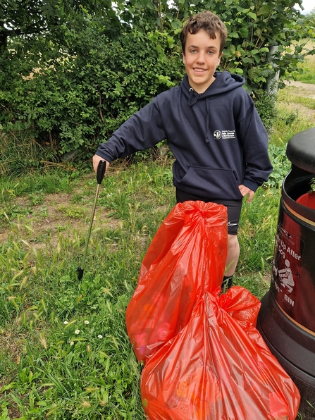 Alex by a bin, with a bag of litter, smiling at the camera