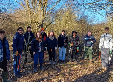 Members from the Young People's Forum standing in a woodland holding work tools and smiling at the camera