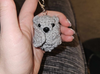 A grey crocheted bat, with wings folded inwards.