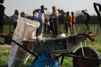 Wheelbarrow with gloves and tools in foreground with blurred images of people in the background