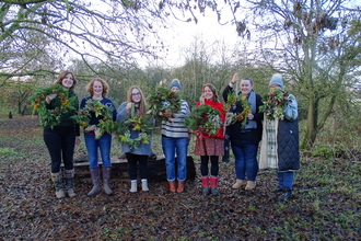 Seven ladies standing outside in winter under trees holding wreaths they've made