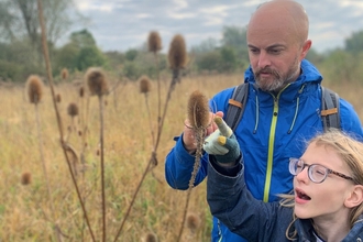Rev'd Chad Chadwick and young person pointing at a teasel in a grassy field at Strawberry Hill