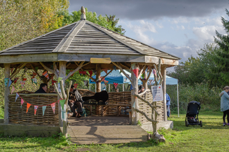 People sit in a wooden outdoor pavilion bedecked with multicoloured bunting