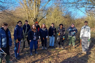 A group of young people with conservation tools smile at the camera