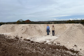Two people standing in front of a newly dug E-shaped bank that is as tall as they are