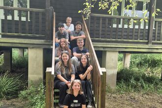 Eight young people sitting on the steps leading up to Rothechilds bungalow.