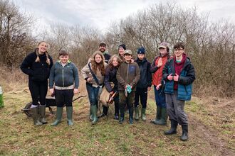 A group of young youth rangers standing together in front of some trees on grass posing for a photo with the reserves officers.