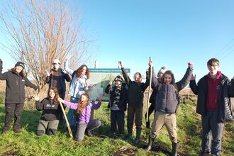 Diverse group of young people with shovels stand outside a nature reseve, smiling at the camera