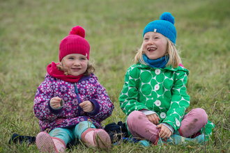 Two children wearing brightly coloured hats and coats siting on grass with binoculars at their side credit Matthew Roberts