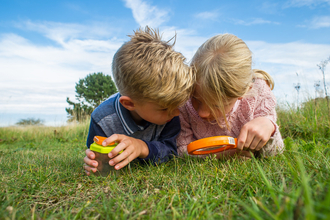 Children laying on grass looking down through magnifying glass