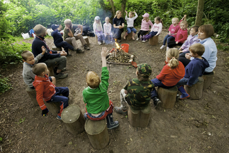 Circle of children and adults sitting on logs around a fire