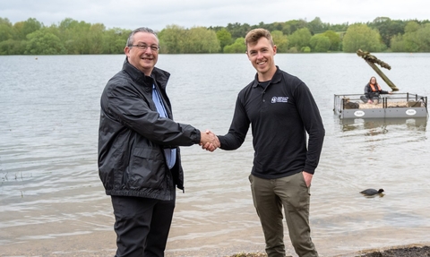Two adults shaking hands in front of the lake where tern rafts are being launched