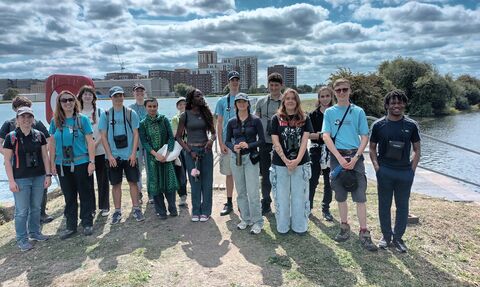 A group of diverse young people stood together, gathered infront of a body of water