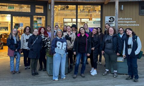 A big group of women are gathered together in front of the Nene Wetlands Visitor Centre, smiling. 