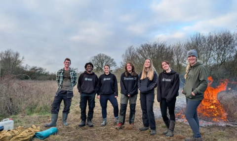 A group of six trainees stand with a reserves officer in front of a fire at Strawberry Hill