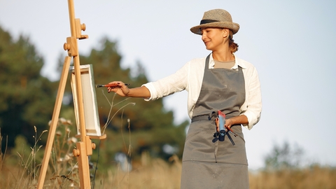 Happy woman in hat painting on canvas in field