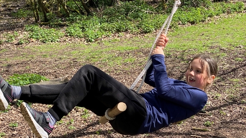 Young white girl wearing black joggers and navy long sleeve tshirt in on a rope swing hanging from a tree