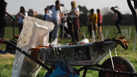 Wheelbarrow with gloves and tools in foreground with blurred images of people in the background