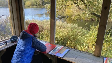 Lady sitting in a hide, looking out to the water with her art materials for journaling