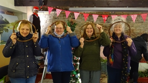 Four ladies stand looking through willow rings they're holding