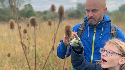 Rev'd Chad Chadwick and young person pointing at a teasel in a grassy field at Strawberry Hill