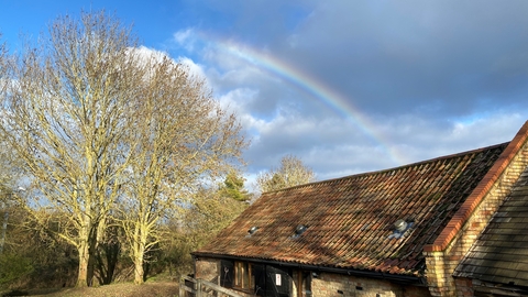 A rainbow shining in blue sky over the low brick building that houses the classroom.
