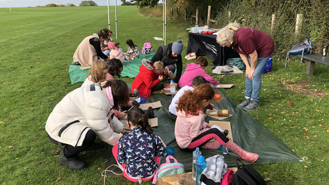 A group of children sit on the floor outside engaged in a wildlife craft activity