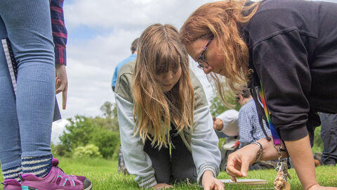 Adult and child kneel to examine plants in the grass