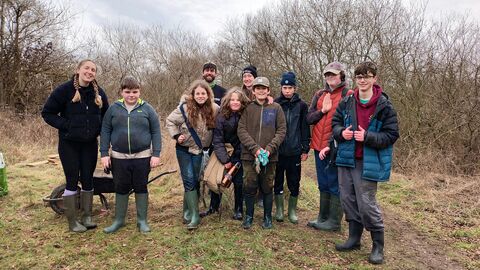 A group of young youth rangers standing together in front of some trees on grass posing for a photo with the reserves officers.