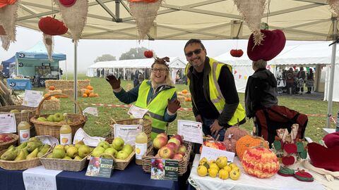 Two people smiling at the camera behind a table of apples.