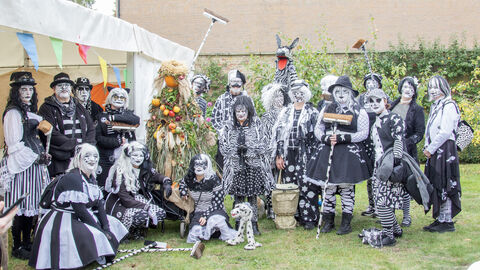 A group of people dressed up in black and white molly dancer attire standing together with a corn queen for a photo.