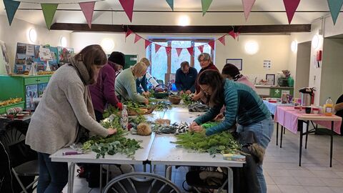 A group of people making willow wreaths using leaves and decorations, on a table in the classroom