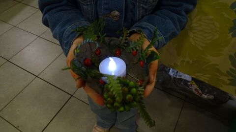 child hands holding a clay candle holder decorated with berries and greenery