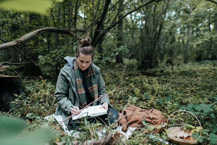 A picture of Agnes Becker seated in a woodland, writing in a journal
