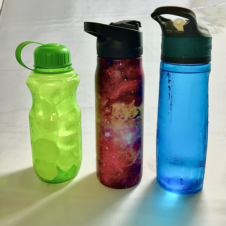 3 water bottles, a green water bottle, next to a red one wrapped in a galaxy image, and then a blue water bottle on the right.
