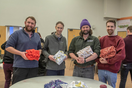 A group of men clutch prettily wrapped gifts with broad smiles on their faces