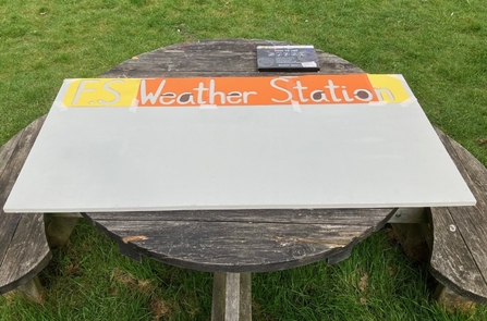 Forest School weather station; a board resting on a wooden table with "F.F Weather Station" on the top.