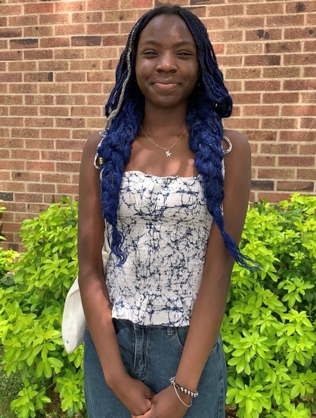 A young Black woman with braided and plaited hair smiles at the camera