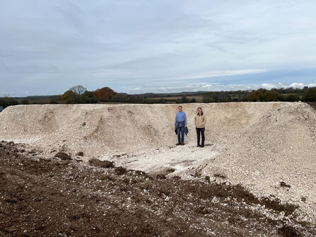 Two people standing in front of a newly dug E-shaped bank that is as tall as they are