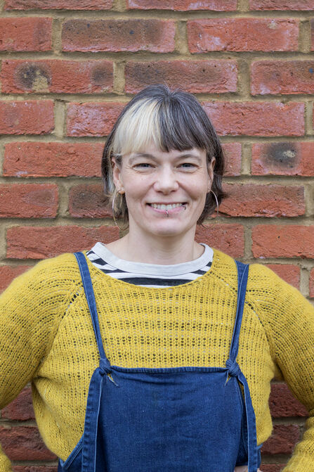 A white woman with short dark hair and a dyed blonde streak smiles at the camera