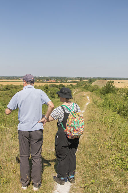 A man and woman stand looking out over a view from, and of, Fleam Dyke