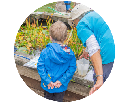 A young boy looks at a pond with an older volunteer showing him something