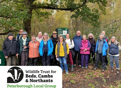 A group of people, wrapped up in outdoor clothing, smiling enthusiastically at the camera, walking through a woodland reserve