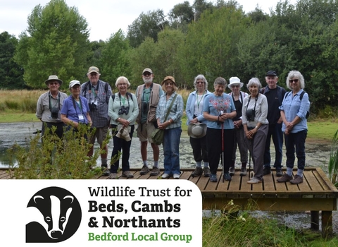 A group of Bedford local group members standing on a wooden boardwalk over wetland, smiling toward the camera