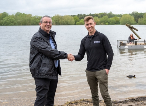 Two adults shaking hands in front of the lake where tern rafts are being launched