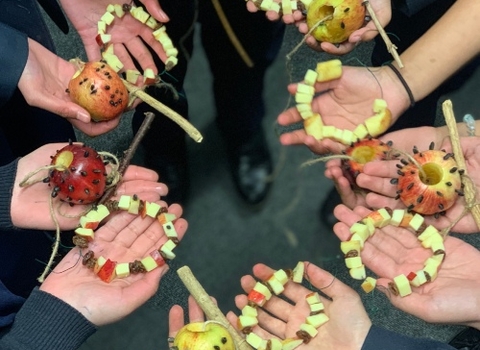 School students hands in a circle, holding natural bird feeders handmade from apples in an activity.