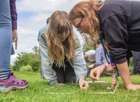 Adult and child kneel to examine plants in the grass